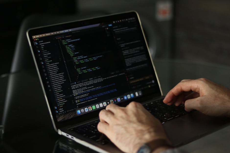 A close-up image of a silver laptop placed on a desk, displaying a software development environment with lines of code on the left side and a large, orange calculator-style interface on the right. The