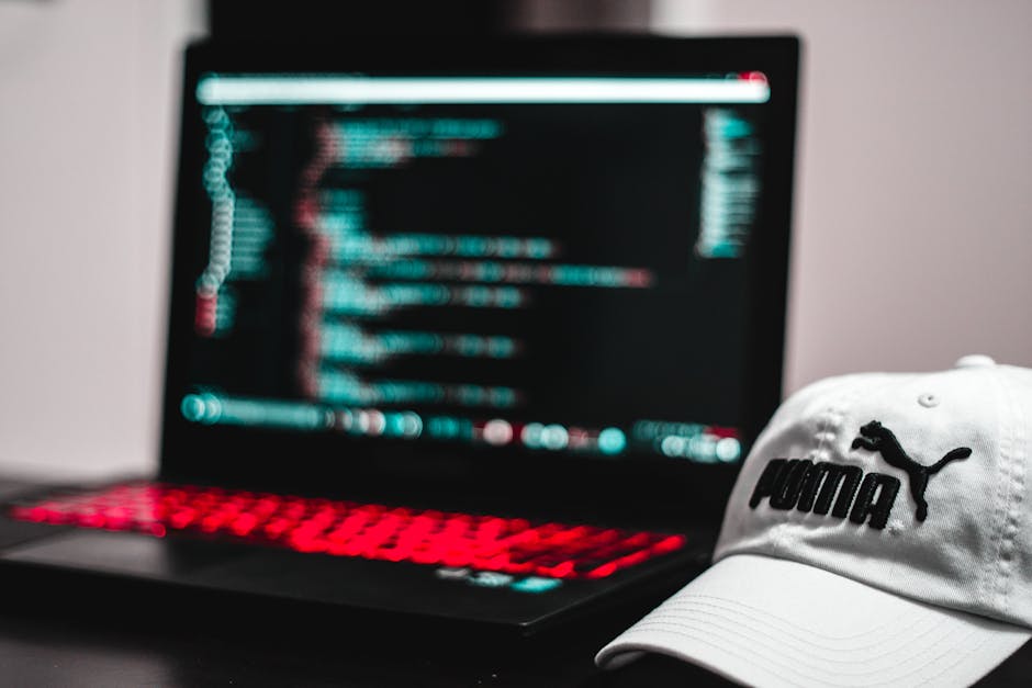 Close-up photograph of a computer screen displaying lines of code in a dark-themed editor, with syntax highlighting in various colors such as green, yellow, and white. The code includes HTML tags, att